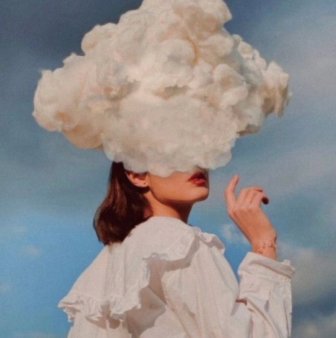 A surreal image of a person with a large, fluffy cloud obscuring their head against a blue sky, evoking a dreamlike or contemplative mood. The individual is dressed in a white, ruffled blouse, enhancing the ethereal aesthetic.