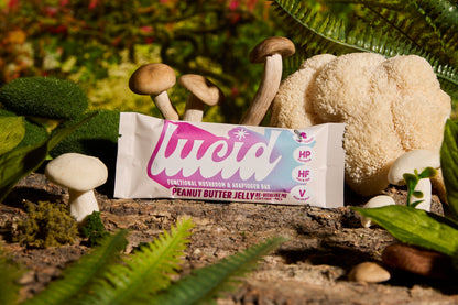 Lucid Peanut Butter and Jelly bar with Lion's Mane and Maca, amid natural greenery and mushrooms, highlights wellness.